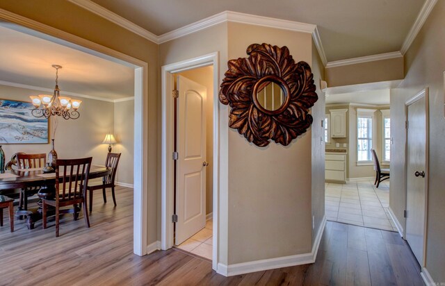 hallway featuring a chandelier, baseboards, light wood-style flooring, and ornamental molding