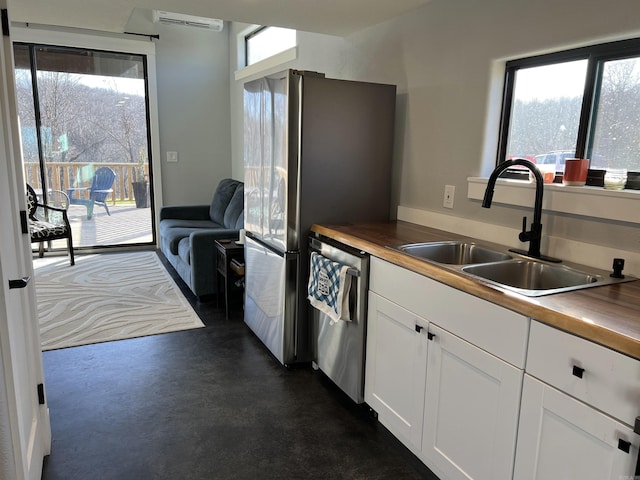 kitchen featuring a wall mounted air conditioner, white cabinetry, stainless steel appliances, and a sink