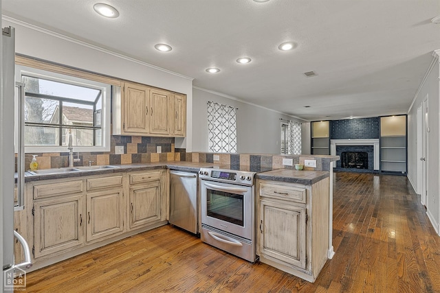 kitchen featuring light brown cabinets, a peninsula, a sink, ornamental molding, and stainless steel appliances