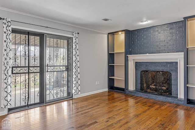 unfurnished living room with visible vents, a brick fireplace, baseboards, ornamental molding, and hardwood / wood-style flooring