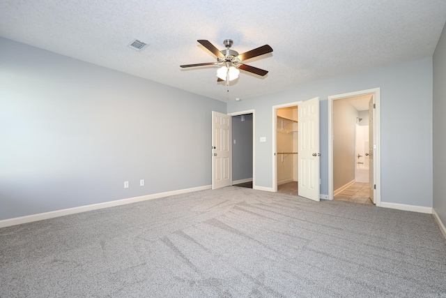 unfurnished bedroom with baseboards, visible vents, a spacious closet, a textured ceiling, and carpet flooring