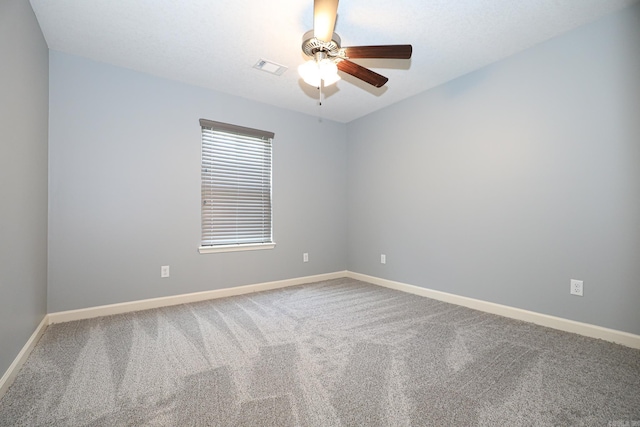 carpeted spare room with visible vents, baseboards, and ceiling fan