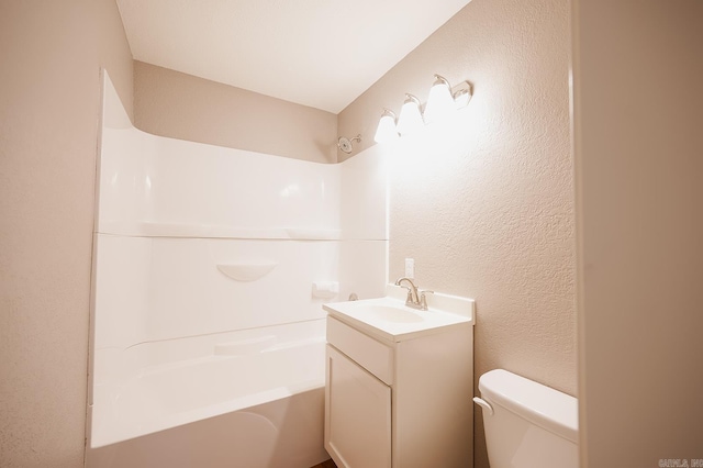 bathroom with tub / shower combination, toilet, vanity, and a textured wall