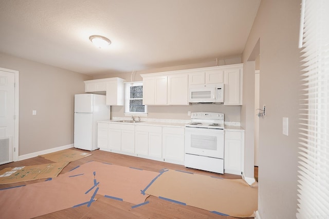 kitchen featuring baseboards, light countertops, white cabinets, white appliances, and a sink