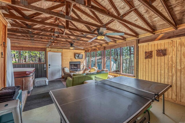 rec room featuring wooden walls, a healthy amount of sunlight, a ceiling fan, and vaulted ceiling