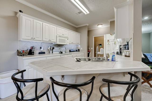 kitchen featuring tile countertops, a breakfast bar, a peninsula, white appliances, and a sink