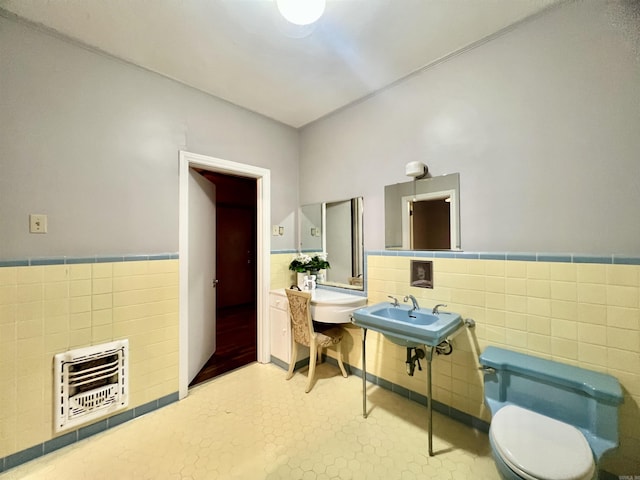 half bathroom with heating unit, a wainscoted wall, a sink, tile walls, and toilet