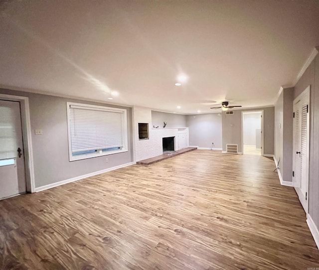 unfurnished living room featuring visible vents, a fireplace with raised hearth, ornamental molding, wood finished floors, and baseboards