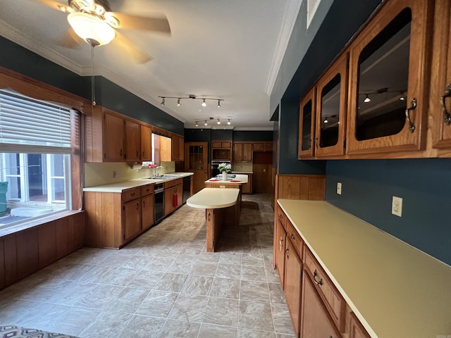 kitchen with ornamental molding, a sink, brown cabinetry, light countertops, and glass insert cabinets