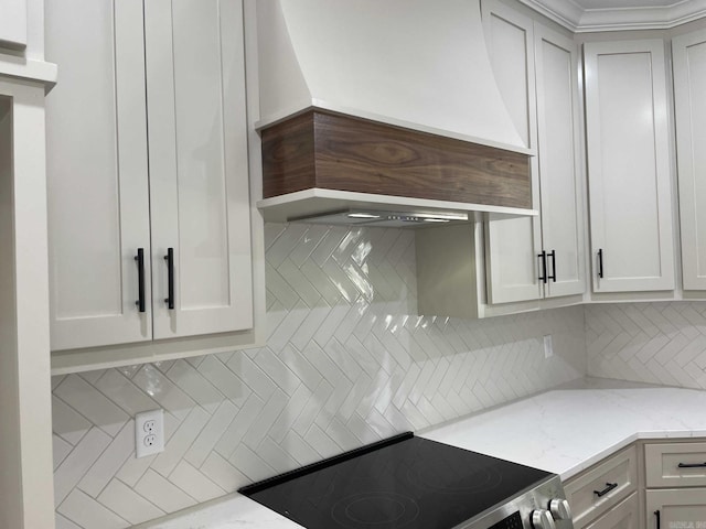 kitchen with tasteful backsplash, light stone countertops, premium range hood, electric range, and white cabinets