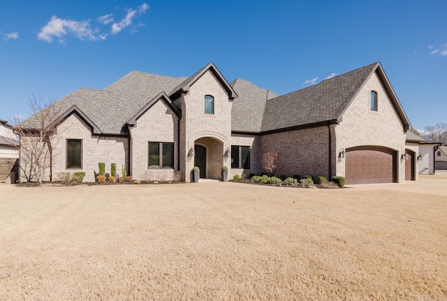 french provincial home featuring brick siding, concrete driveway, and a garage