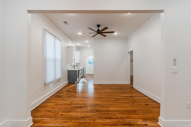 unfurnished living room featuring wood finished floors, visible vents, a ceiling fan, baseboards, and ornamental molding