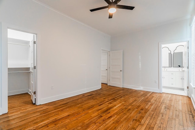 unfurnished bedroom with baseboards, a spacious closet, hardwood / wood-style floors, and crown molding