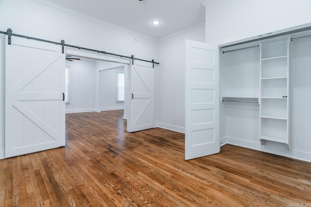 interior space featuring a closet, wood finished floors, a barn door, and ornamental molding