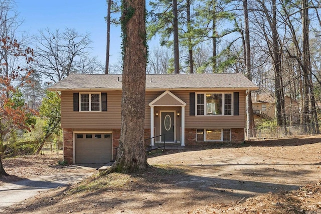 bi-level home with brick siding, concrete driveway, fence, and a garage