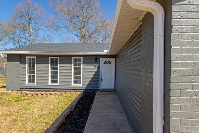 doorway to property with brick siding and roof with shingles