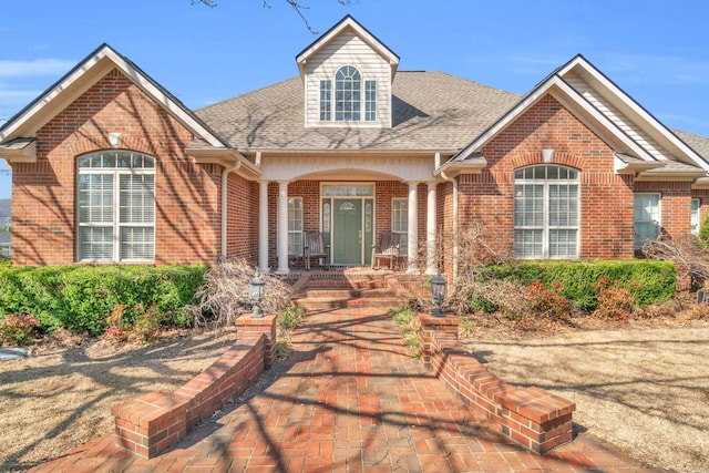 view of front facade with a porch, brick siding, and a shingled roof