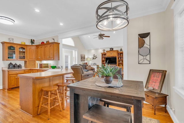 dining space with light wood finished floors, baseboards, vaulted ceiling, ornamental molding, and a ceiling fan