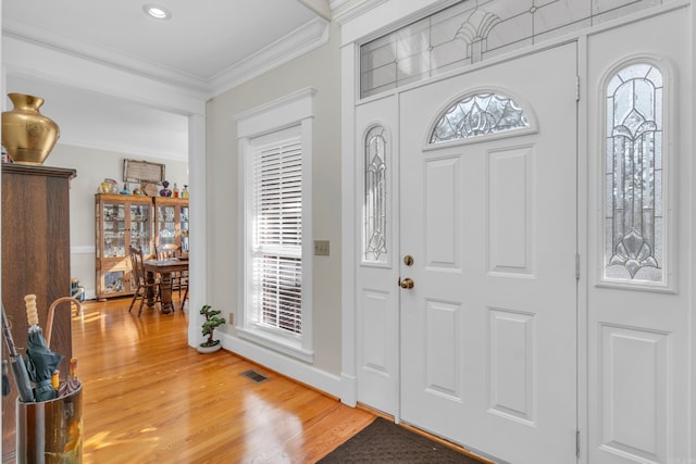 entrance foyer with crown molding, plenty of natural light, visible vents, and light wood-type flooring