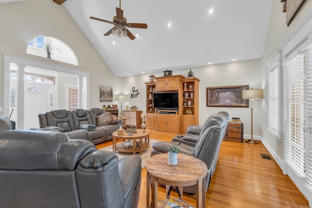 living area featuring visible vents, light wood-style floors, high vaulted ceiling, and ornate columns