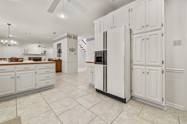 kitchen with light tile patterned floors, a fireplace, white cabinets, white refrigerator with ice dispenser, and ceiling fan with notable chandelier