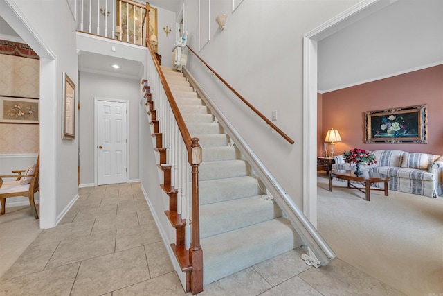 stairway with tile patterned floors, baseboards, a towering ceiling, and crown molding