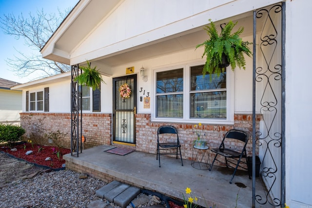 entrance to property featuring a porch and brick siding