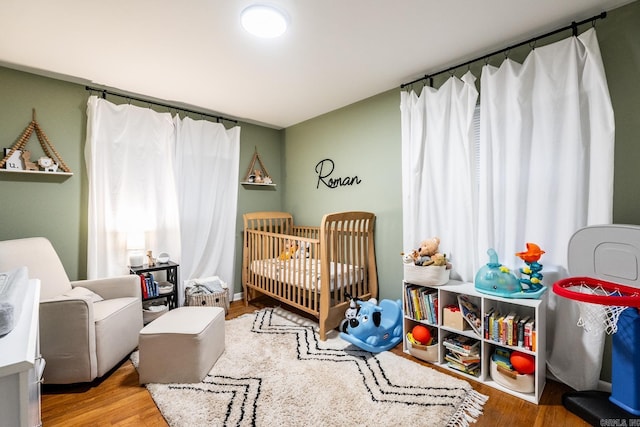 bedroom with a nursery area and wood finished floors