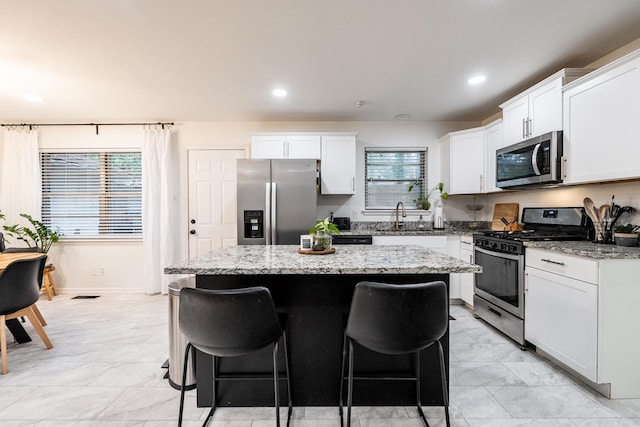 kitchen with a sink, appliances with stainless steel finishes, white cabinetry, a kitchen breakfast bar, and a center island