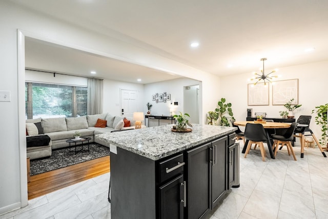 kitchen featuring a center island, light stone counters, hanging light fixtures, a notable chandelier, and dark cabinets