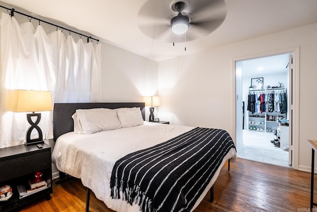 bedroom with a spacious closet, dark wood-type flooring, and a ceiling fan