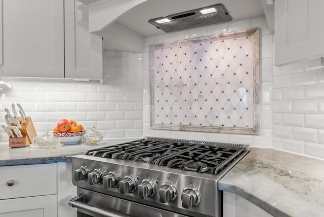 kitchen with stainless steel gas range oven, arched walkways, backsplash, and white cabinetry