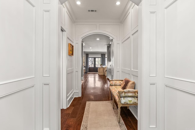 hall with dark wood-style floors, visible vents, recessed lighting, arched walkways, and a decorative wall