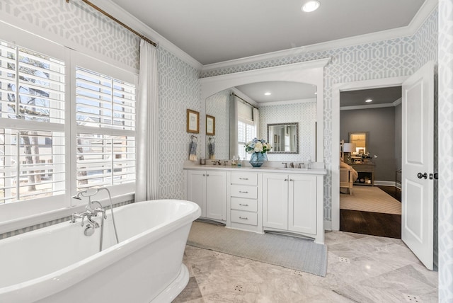 full bathroom with wallpapered walls, double vanity, ornamental molding, a soaking tub, and a sink