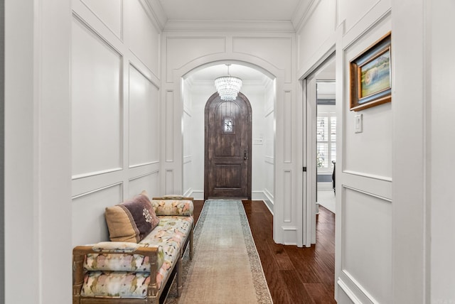 foyer featuring a decorative wall, arched walkways, dark wood-style flooring, and ornamental molding