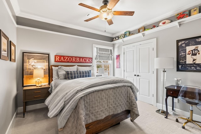 carpeted bedroom with a closet, ceiling fan, baseboards, and ornamental molding