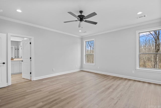 empty room with light wood-type flooring, visible vents, baseboards, and crown molding