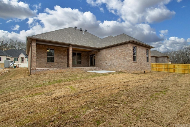 rear view of house featuring brick siding, fence, roof with shingles, a yard, and a patio