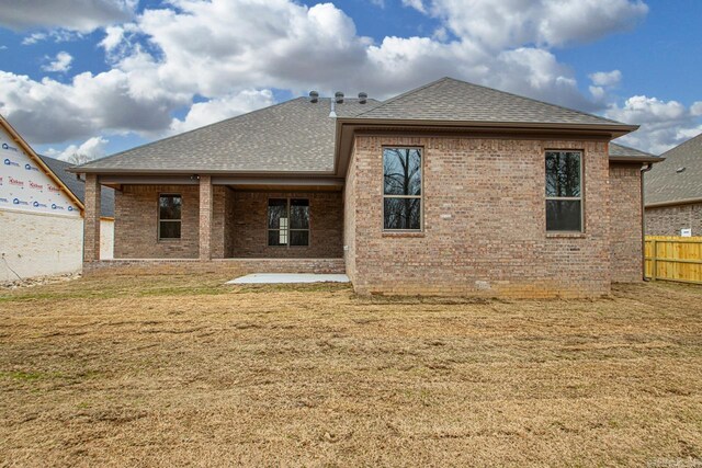 rear view of house featuring a patio area, roof with shingles, brick siding, and fence