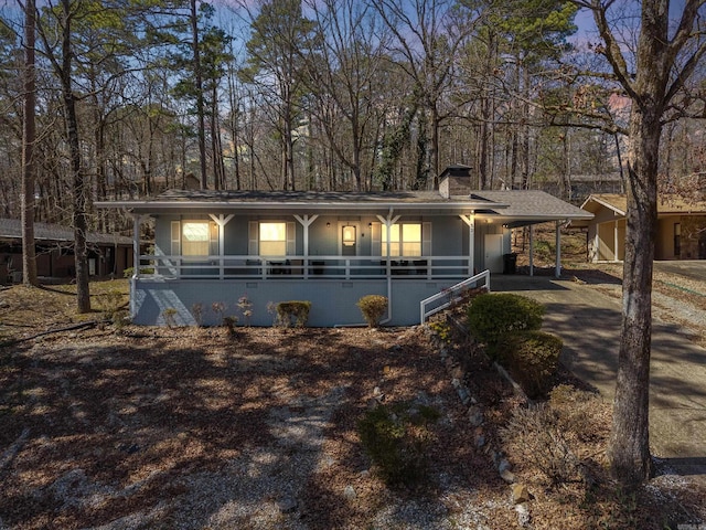 view of front facade featuring a carport, covered porch, driveway, and a chimney