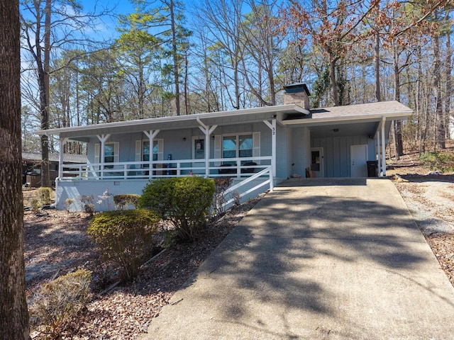 view of front of property with board and batten siding, covered porch, a chimney, a carport, and driveway