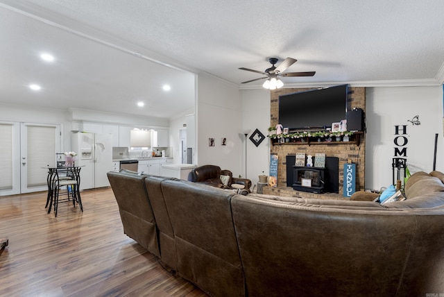 living area with a ceiling fan, light wood-style flooring, recessed lighting, ornamental molding, and a textured ceiling