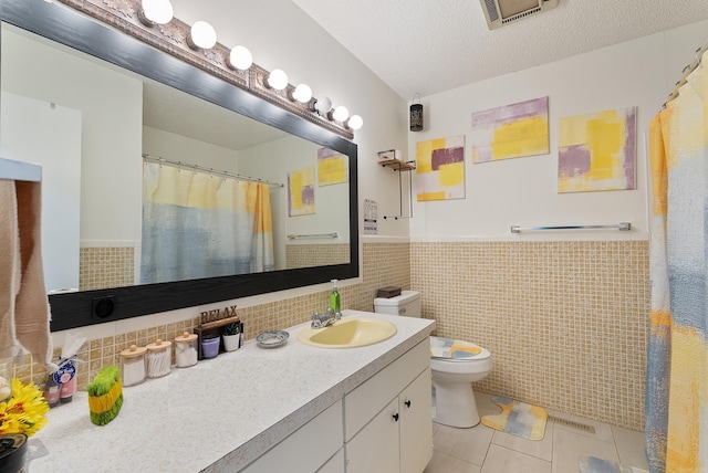 full bathroom featuring tile patterned floors, visible vents, a wainscoted wall, toilet, and a textured ceiling