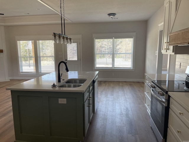 kitchen featuring a center island with sink, a sink, wood finished floors, stainless steel appliances, and light countertops