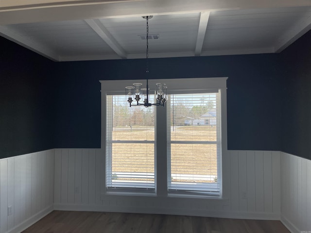 unfurnished dining area with beamed ceiling, a healthy amount of sunlight, and wood finished floors