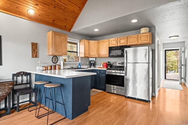 kitchen featuring a sink, stainless steel appliances, a peninsula, light wood finished floors, and lofted ceiling