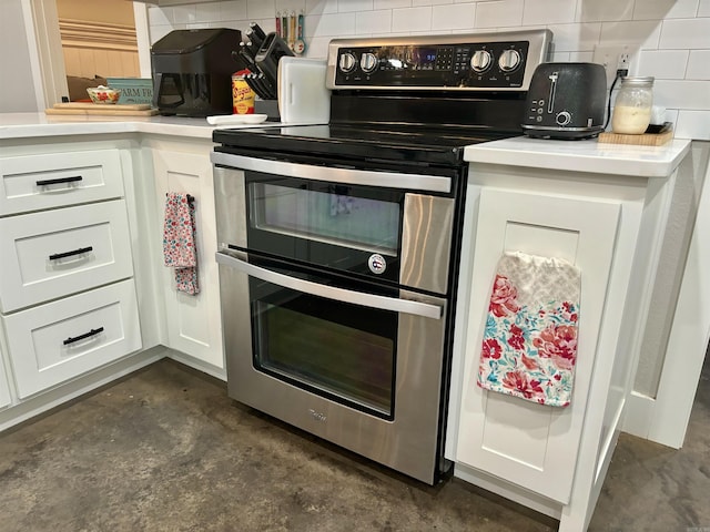 kitchen with double oven range, concrete floors, decorative backsplash, and white cabinetry