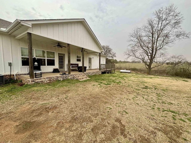 rear view of property featuring a lawn, a ceiling fan, board and batten siding, a wooden deck, and a patio area