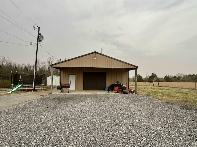 detached garage with a trampoline, driveway, and fence