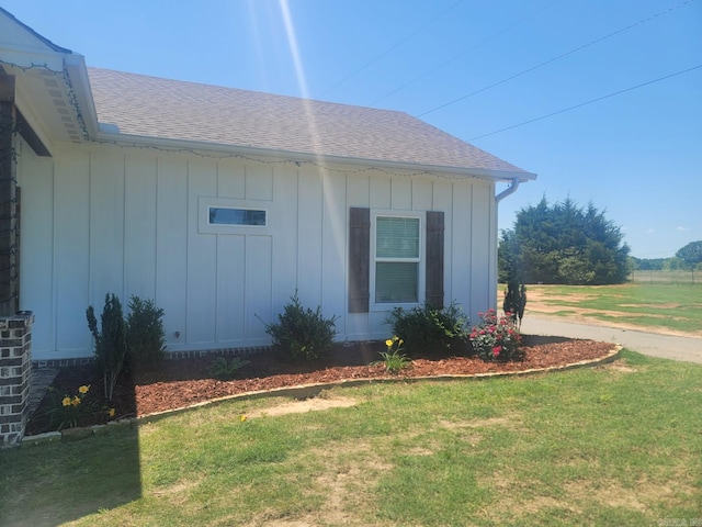 view of side of home featuring a yard, board and batten siding, and a shingled roof